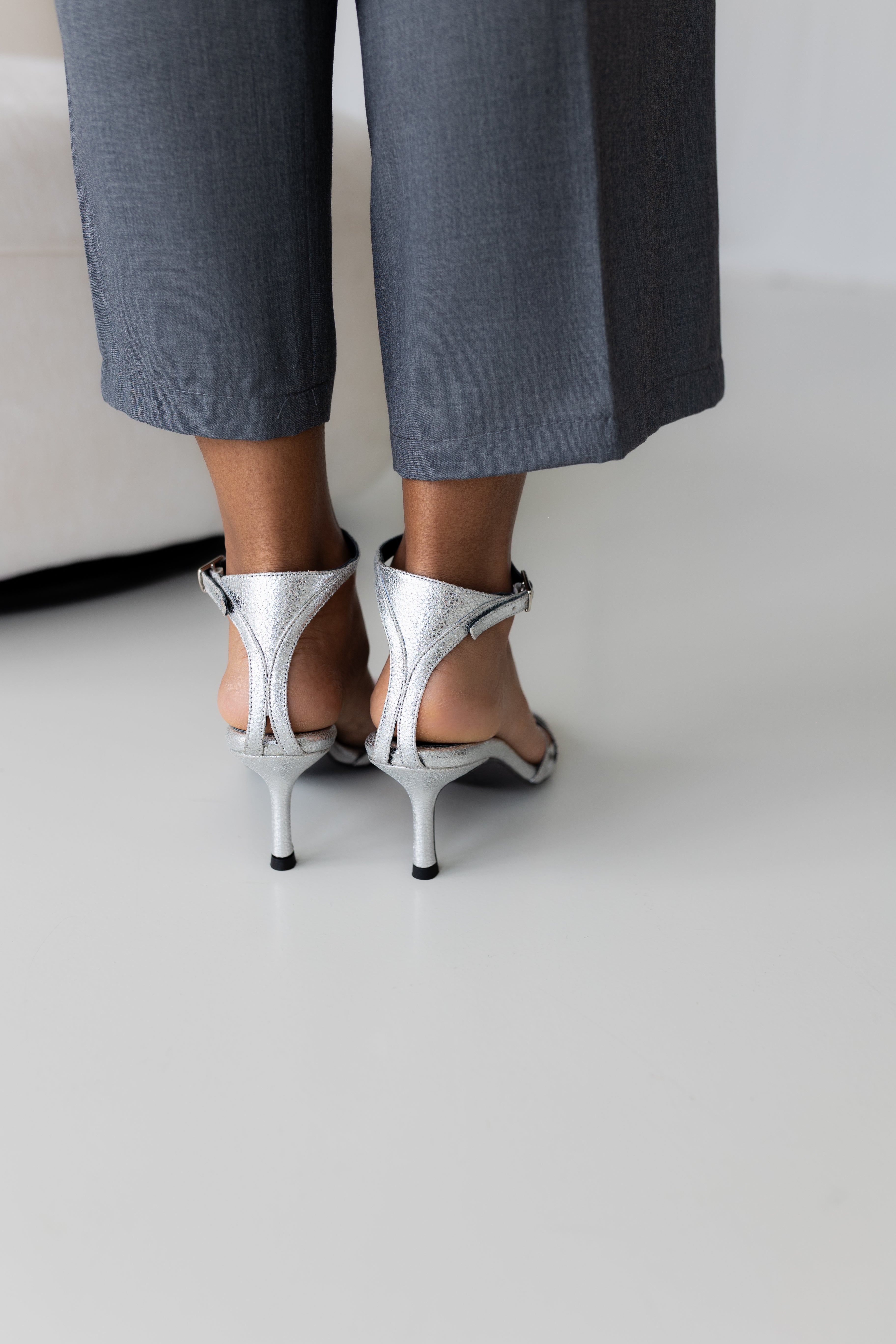 Sandalia elegante de mujer en piel plata con correa al tobillo.