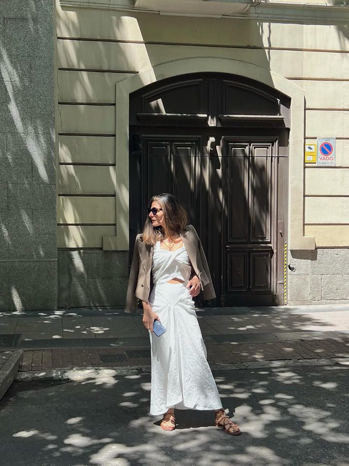 Mujer posando con vestido blanco y sandalias planas de tiras en piel marrón
