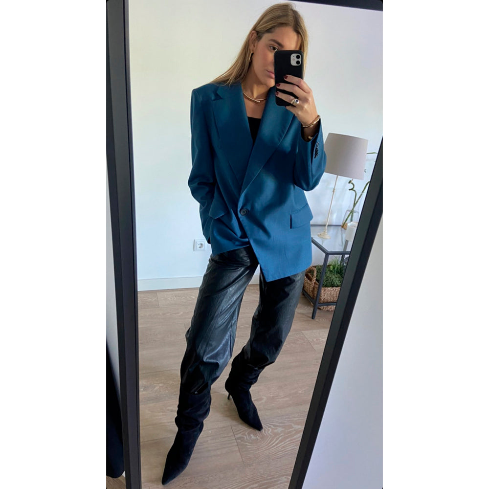 Mujer rubia con chaqueta azul, pantalones de cuero negros y botines de tacón a juego