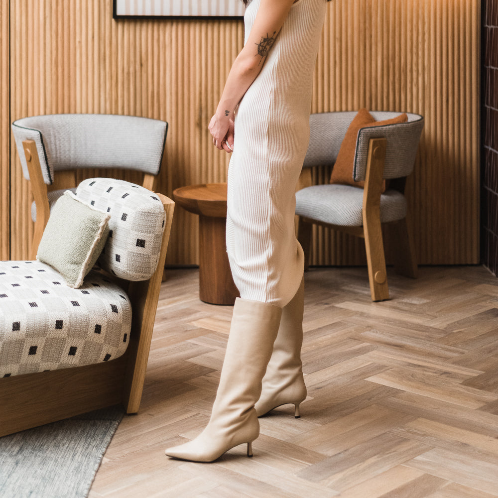 Mujer posando de perfil con botas de tacón y caña alta y vestido conjuntado en color nude