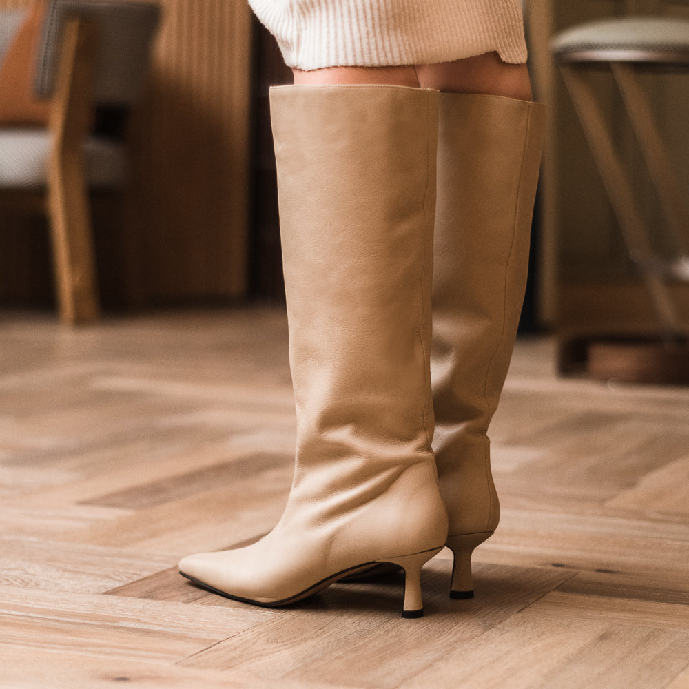 Vista izquierda trasera de botas con tacón, altas de caña y hechas en piel color nude