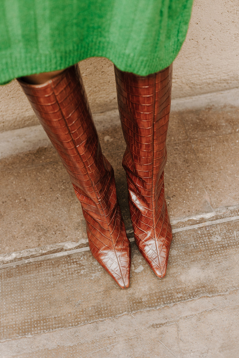 Vista de frente de una chica con botas de tacón y caña alta efecto cocodrilo en piel marrón