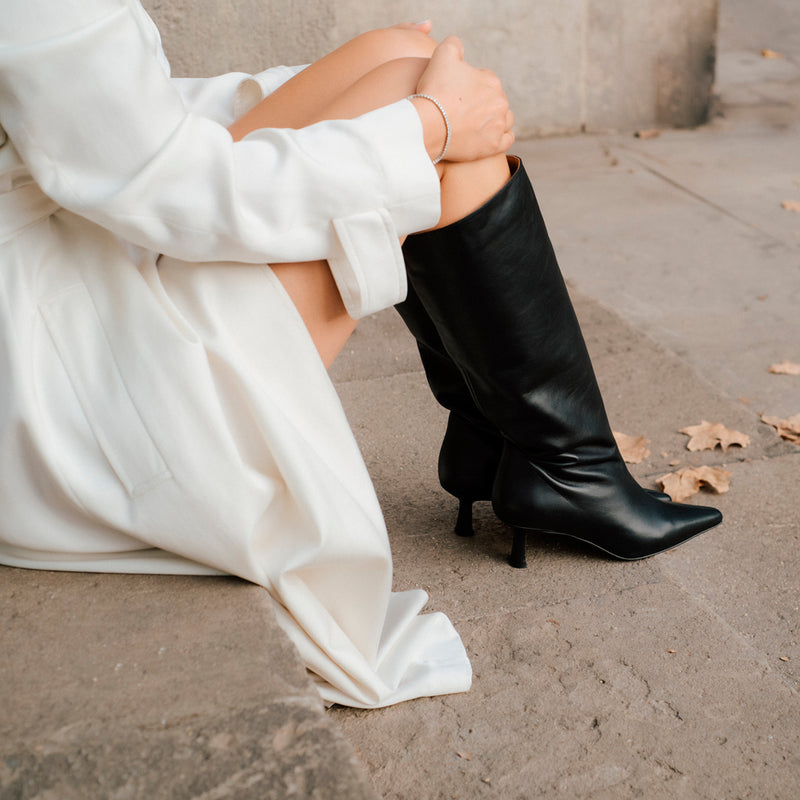 Mujer sentada con abrigo blanco y un par de botas altas en piel color negro