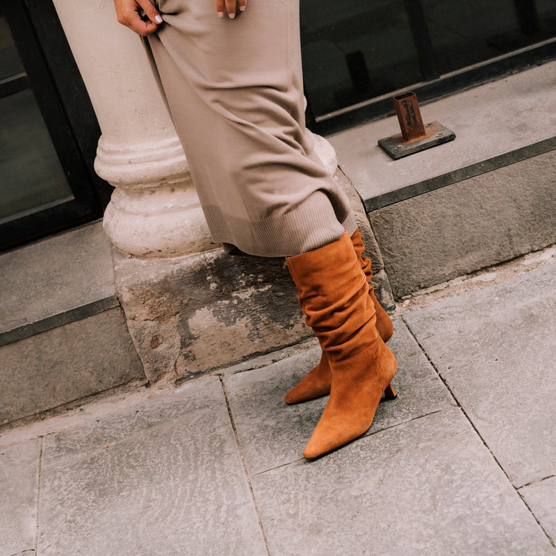 Mujer posando de lado con unos botines en ante marrón con tacón midi muy cómodos perfecto para llevar durante todo el día.