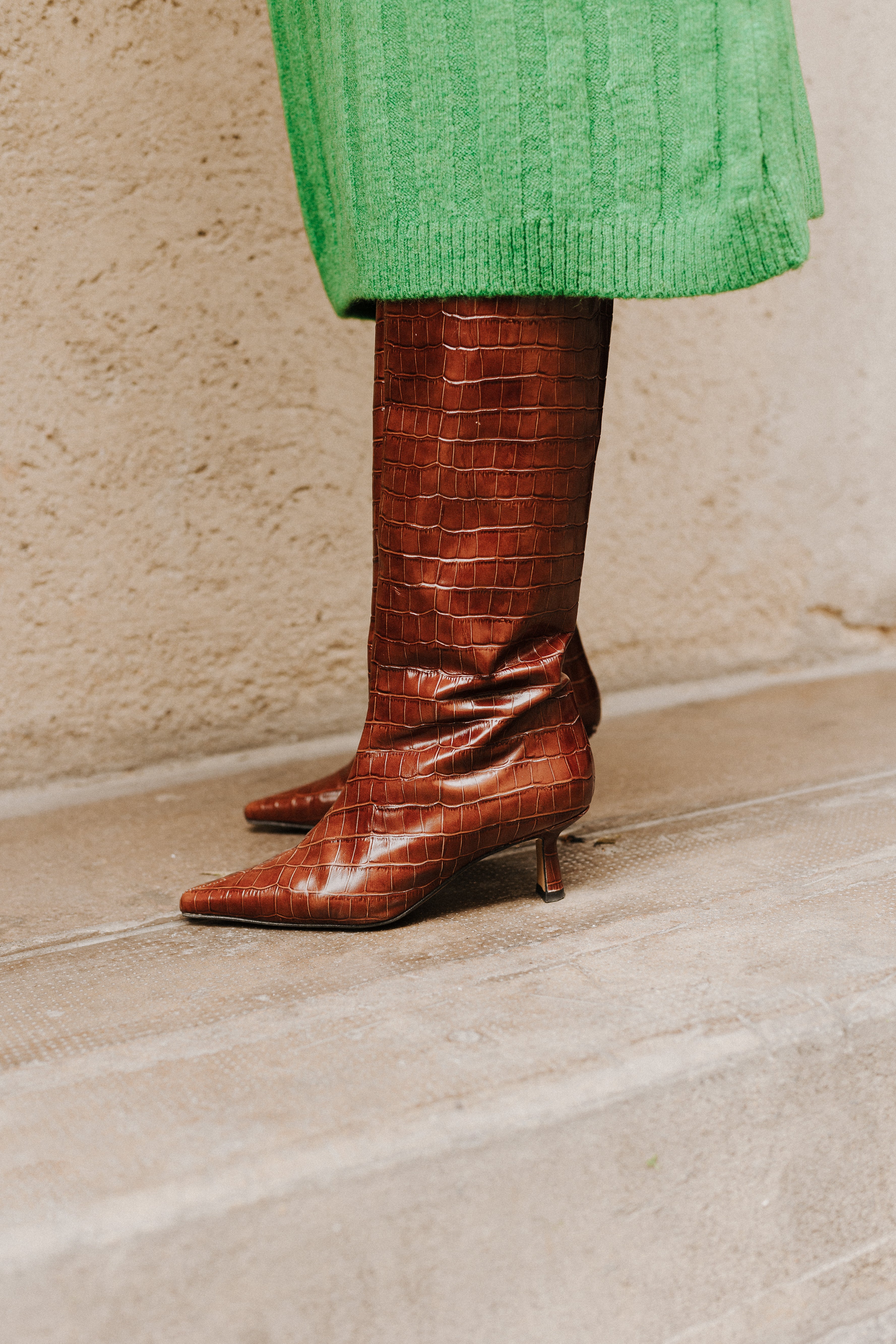Mujer posando de perfil con un vestido verde largo y unas botas de tacón marrones efecto cocodrilo